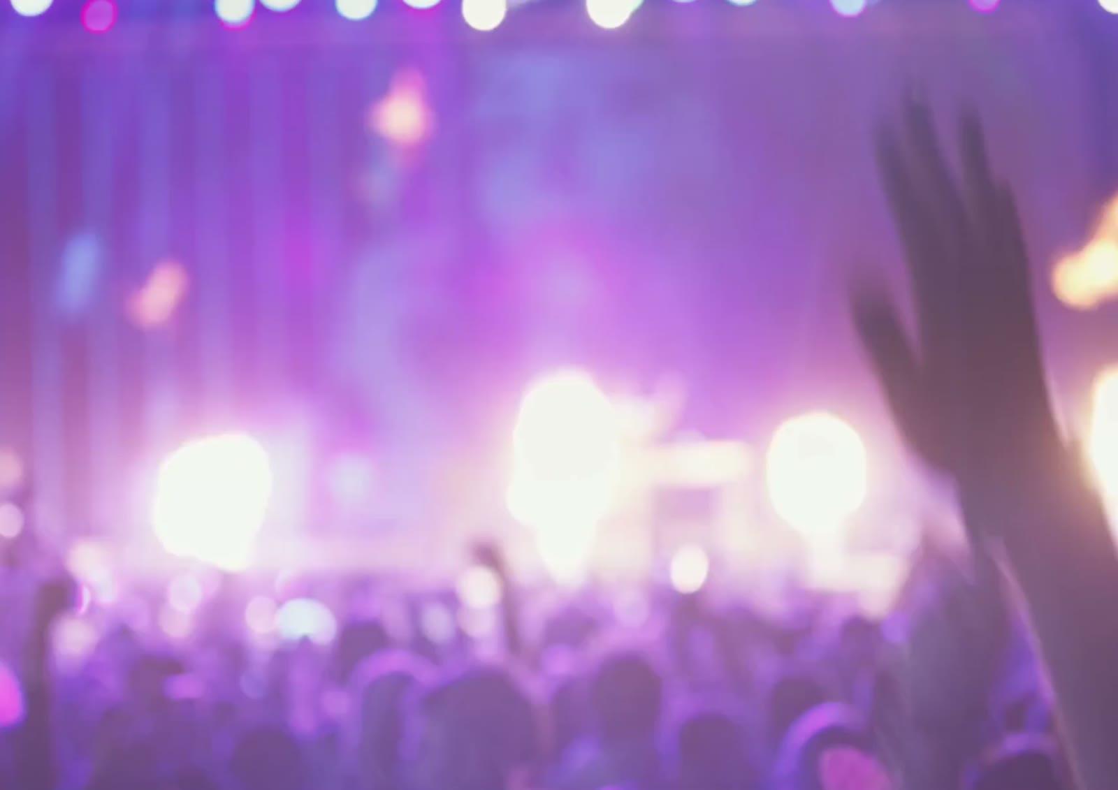 A crowd sharing a live event under purple stage lights